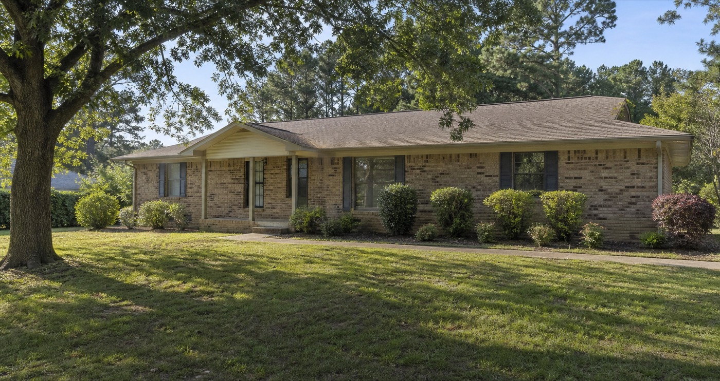 Modest East Texas brick ranch home with mature trees and a front lawn